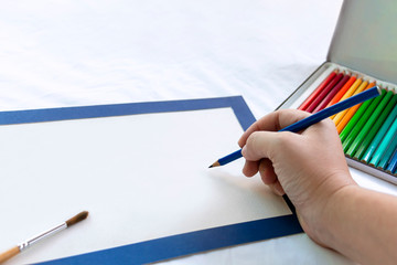 Woman's hand holding colorful pencils for drawing art and brush for painting on blank paper on table background. Concept education with copy space for text.