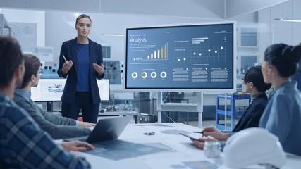 Wall Mural - Modern Industrial Factory Meeting: Confident Female Engineer Uses Interactive Whiteboard, Makes Report to a Group of Engineers, Managers Talks and Shows Statistics, Growth and Analysis Information