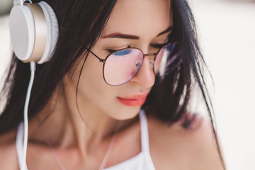 Beautiful young girl with brunette  hair listening to music on headphones, street style, outdoor portrait, hipster girl, music, mp3, Bali, beauty woman, sunglasses, orange color, concept, glasses