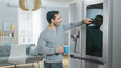 © Gorodenkoff - Handsome Young Man is Standing Next to a Refrigerator While Drinking His Morning Coffee. He is Checking a To Do List on a Smart Fridge at Home. Kitchen is Bright and Cozy.