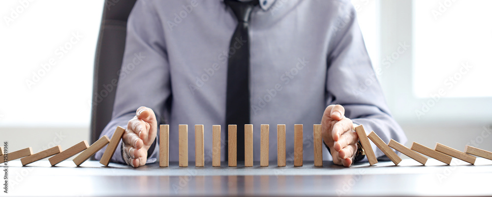 business man blocks falling blocks with his hands to prevent domino effect - obrazy, fototapety, plakaty 