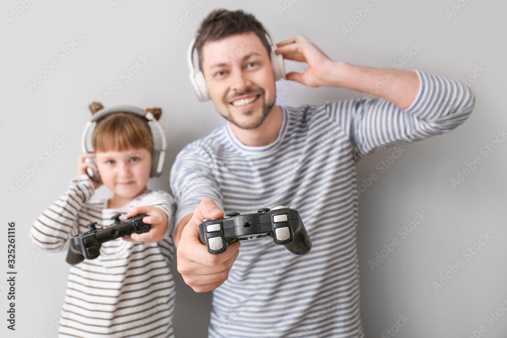 Father and his little daughter playing video games on grey background