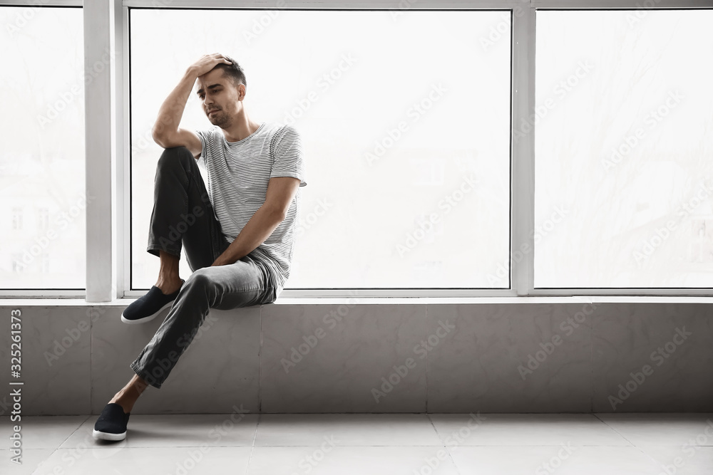 Depressed young man near window