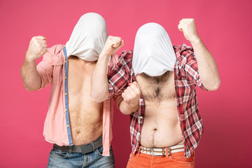 Two stupid men, for the sake of a joke, covered their heads with their tee-shirts, compared their stomachs and showed biceps. On a red background.