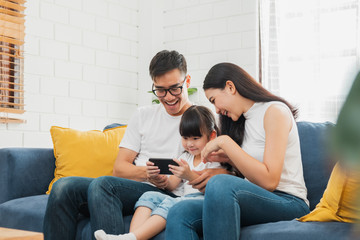 Happy Asian family using tablet, laptop, phone for playing game watching movies, relaxing at home for technology lifestyle concept