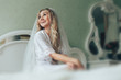 The bride is sitting on the bed in her bedroom in the morning. Beautiful blonde girl with a veil sitting on the bed