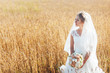 A beautiful young bride stands in a field of wheat at sunset.
