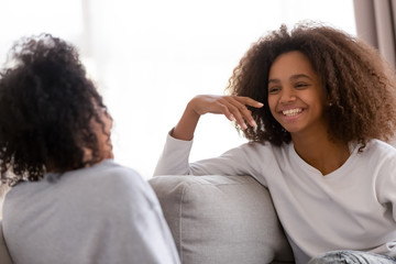 Wall Mural - Happy african mother and daughter talking laughing sitting on sofa