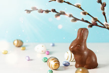 Golden Easter Eggs, Chocolate Easter Bunny And Spring Tree Branches Over Blue Background.