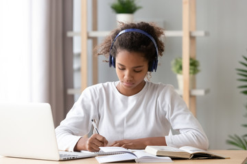 Wall Mural - Focused african african teen girl wearing headphones writing notes studying
