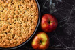 European apple pie with topping crumbles in springform pan on right side and blank copy space on black marbel background to left side
