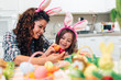 © hedgehog94 - A mother and her cute daughter are painting colorful eggs and wearing bunny ears. Happy family are preparing for Easter.