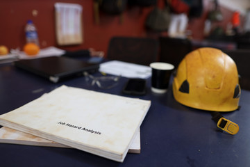 Wall Mural - job hazard analysis risk assessment book placing on the table with yellow hard hat computer at the b