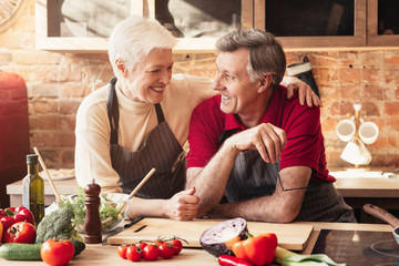 Wall Mural - Happy elderly couple embracing in kitchen while cooking dinner together