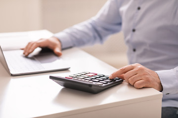 Senior man using laptop and calculator at office