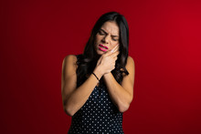 Young Pretty Latin Woman With Tooth Pain On Red Studio Background. Toothache, Dental Problems, Stomatology And Medicine Concept.
