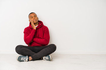 Young latin man sitting on the floor isolated who is bored, fatigued and need a relax day.