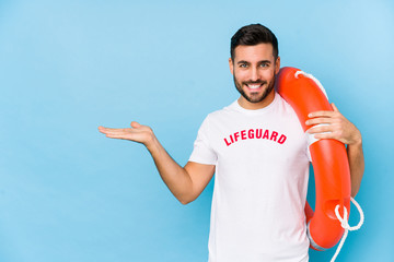 Wall Mural - Young handsome lifeguard man isoalted showing a copy space on a palm and holding another hand on waist.