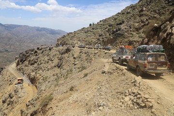 Citizens transport their needs in rugged roads due to Al-Houthi militia blockade of the main roads of Taiz city .