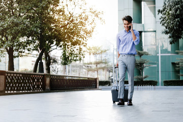 Happy Young Businessman Using Mobile Phone while Walking with Suitcase in the City. Lifestyle of Modern People. High Angle View. Full Length