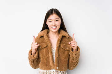 Wall Mural - Young chinese woman posing in a white background isolated indicates with both fore fingers up showing a blank space.