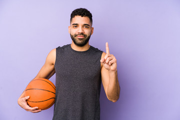 Wall Mural - Young latin man playing basket isolated showing number one with finger.