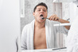 a man in a white coat brushing his tongue with a toothbrush through a bathroom mirror.