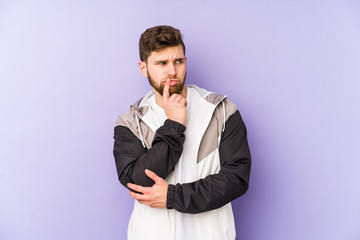 Wall Mural - Young man isolated on purple background looking sideways with doubtful and skeptical expression.