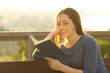 © Antonioguillem - Happy woman reading a book sitting on a bench outdoors