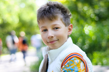 Handsome young boy portrait. Smiling kid boy looking at camera on the street on green nature background. Little boy, child outdoors in summer or spring.