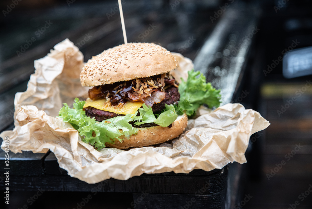 Obraz na płótnie Duży burger w amerykańskim stylu na drewnianym blacie. Kanapka z grillowanym mięsem ze świeżymi warzywami i serem. Hamburger owinęty w papier ekologiczny podany na wynos w salonie