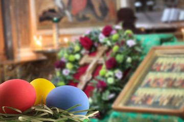 Three painted chicken eggs, red, yellow and blue, lie in a nest of straw in the temple room on a blurred background.  Easter. Selective focus