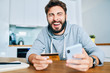 © baranq - Young man screaming in joy while shopping online with smartphone and credit card