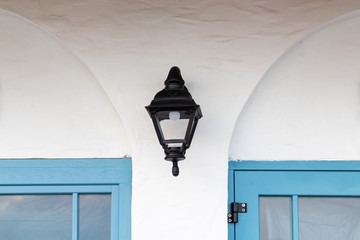 Vintage old street classic black iron outdoor lantern, lamp on white house wall between two blue window frames