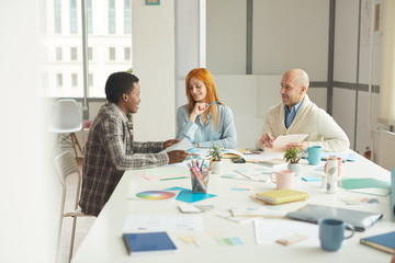 Wall Mural - Portrait of mature business people smiling cheerfully while talking to African-American intern during interview meeting in modern white office, copy space