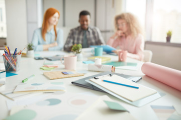 Wall Mural - background image of note pad with pencil and office supplies on table with creative team in backgrou