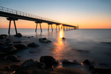 Fototapeta Morze - View of a sea dock at dawn from the beach with long exposure creating a silky smooth water
