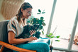 © Valerii Apetroaiei - An attractive young woman in glasses is working on a laptop while sitting cross-legged in a comfortable chair at home with a funny assistant cat on her legs.