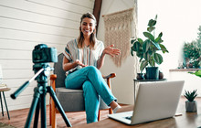 Attractive Young Woman Blogger Dressed In Jeans And A Blouse Is Recording On The Camera While Sitting On A Comfortable Chair At Home.