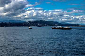 A convoy of tugboats and barges in the Strait of Georgia goes to the shore of Vancouver Island in the port of Nanaimo on the front of the main ridge and stormy sky 