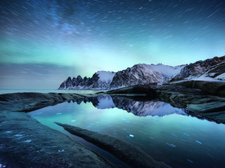 Wall Mural - Tungeneset rocks and Aurora Borealis light. Stars trails and northern light. Reflections on the water surface. Senja islands, Norway. Travel - image