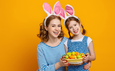 Wall Mural - Happy easter! family mother and child daughter with ears hare getting ready for holiday on colored yellow background.