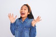 © Krakenimages.com - Young beautiful chinese woman wearing denim shirt standing over isolated white background celebrating crazy and amazed for success with arms raised and open eyes screaming excited. Winner concept