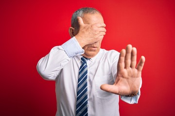 Sticker - Senior handsome businessman wearing elegant tie standing over isolated red background covering eyes with hands and doing stop gesture with sad and fear expression. Embarrassed and negative concept.