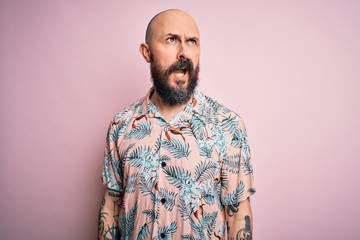 Poster - Handsome bald man with beard and tattoo wearing casual floral shirt over pink background angry and mad screaming frustrated and furious, shouting with anger. Rage and aggressive concept.