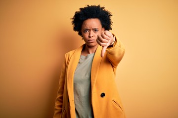 Wall Mural - Young beautiful African American afro businesswoman with curly hair wearing yellow jacket looking unhappy and angry showing rejection and negative with thumbs down gesture. Bad expression.