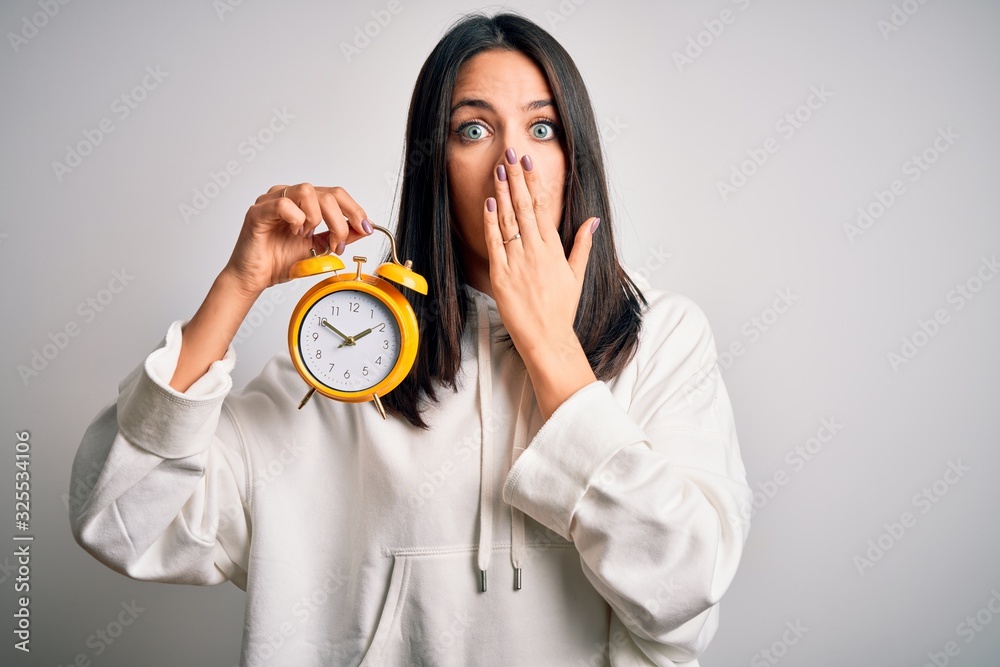 Young woman with blue eyes holding alarm clock standing over isolated ...