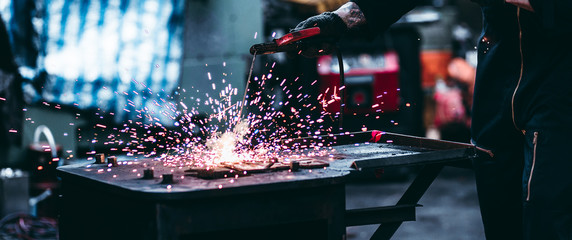 Electric wheel grinding on steel structure in factory, worker with protective mask welding metal and sparks