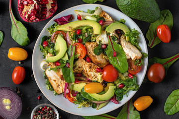 Wall Mural - Healthy salad with grilled chicken breast, avocado, pomegranate seeds and tomato on black background. healthy diet food