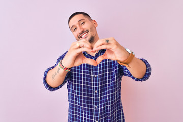 Wall Mural - Young handsome man standing over isolated background smiling in love doing heart symbol shape with hands. Romantic concept.